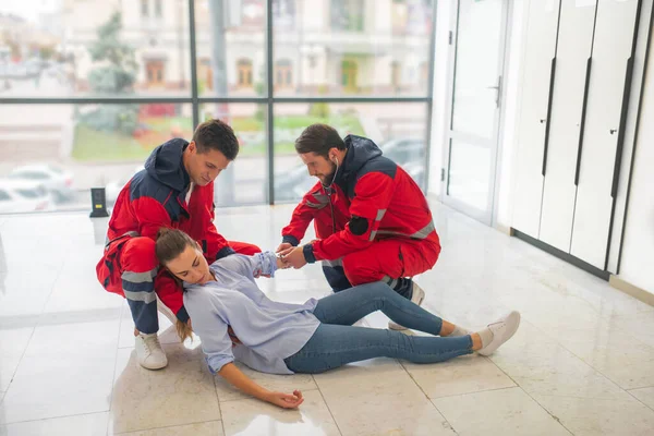 Kırmızı üniformalı iki tıp işçisi baygın bir kadına iğne yapıyor. — Stok fotoğraf