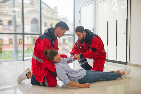 Dos trabajadores médicos en uniforme rojo deteniendo a una mujer débil —  Fotos de Stock