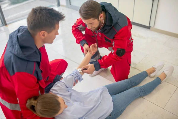 Kırmızı üniformalı iki tıp çalışanı, baygın bir kadını halatla yaralıyor. — Stok fotoğraf