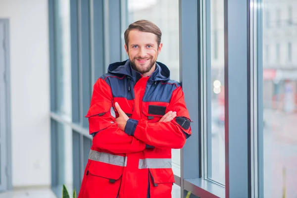 Médico barbudo en uniforme rojo de pie cerca de la ventana — Foto de Stock