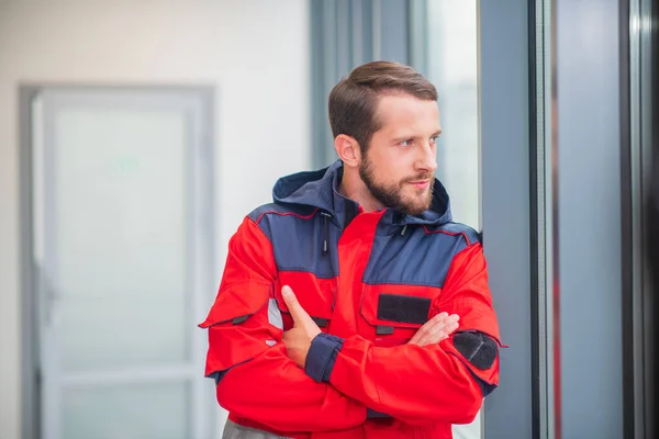 Médico masculino de uniforme rojo de pie cerca de la ventana y con aspecto serio — Foto de Stock