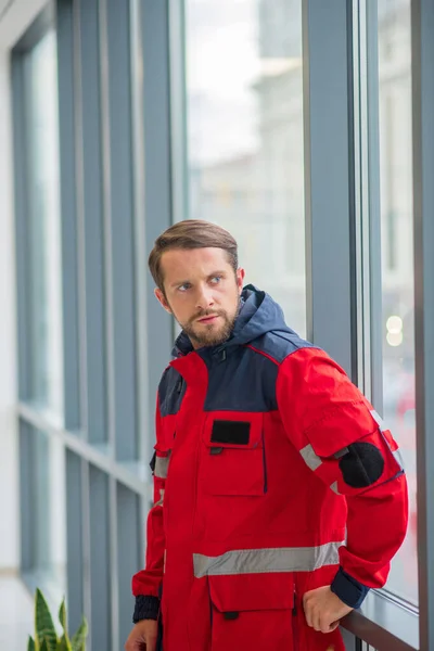 Man arts in rood uniform staan in de buurt van het raam en kijken bezorgd — Stockfoto