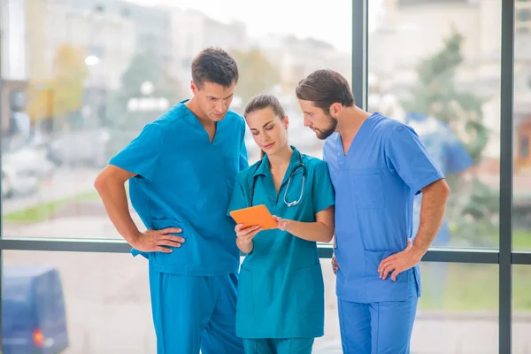 Groep artsen kijken naar iets op tablet en kijken betrokken — Stockfoto