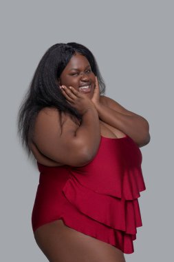 Kırmızı iç çamaşırlı, gülümseyen ve yanaklarına dokunan Afrikalı Amerikalı genç bir kadın.