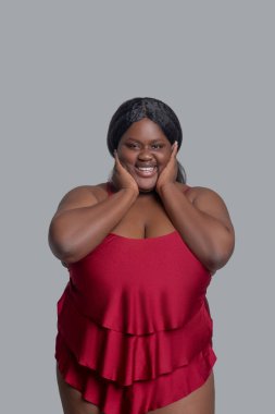 Kırmızı iç çamaşırlı koyu tenli kadın gülümsüyor ve kendinden emin görünüyor.