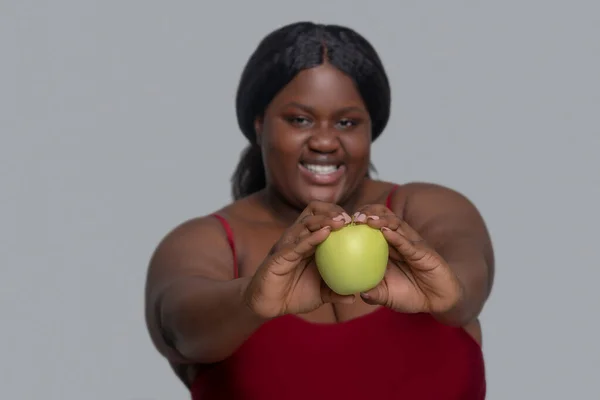 Plus storlek afrikansk amerikansk ung kvinna i rött håller ett äpple och ler — Stockfoto