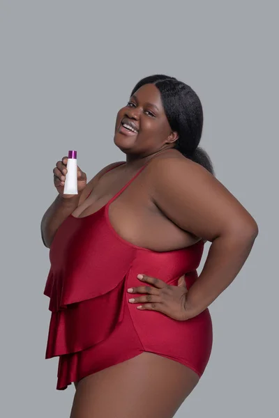 Plus size african american young woman in red holding a tube with cream — Stock Photo, Image