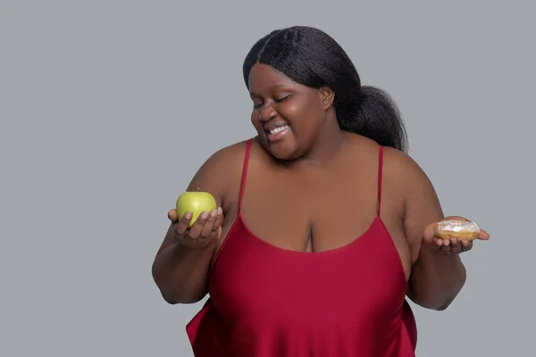 Africano mulher americana com uma maçã e um donuts nas mãos — Fotografia de Stock