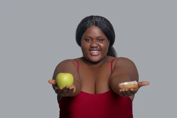 Afroamerykanka z jabłkiem i pączkami w rękach — Zdjęcie stockowe