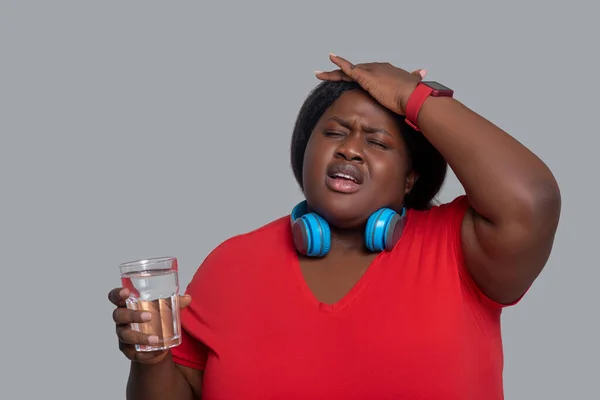 Молодая темнокожая женщина со стаканом воды плохо себя чувствует — стоковое фото