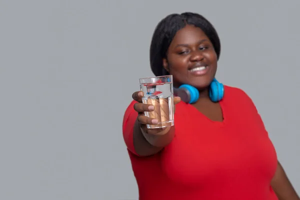 Junge dunkelhäutige Frau mit Kopfhörern hält ein Glas Wasser in der Hand — Stockfoto