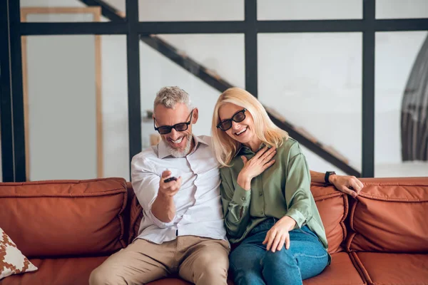 Pareja madura en gafas de sol sentada en el sofá y sintiéndose alegre — Foto de Stock