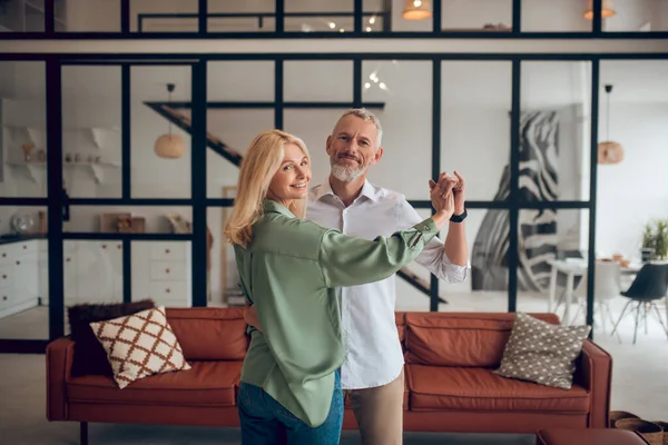 Pareja madura bailando en la habitación y luciendo feliz —  Fotos de Stock