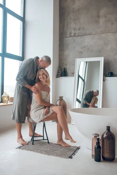 Hombre de pelo gris en bata de baño de pie cerca de la mujer rubia en una toalla —  Fotos de Stock