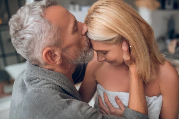 Man met grijs haar zoenen een blonde vrouw met tederheid — Stockfoto