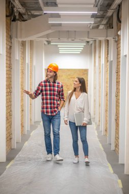 Turuncu kasklı inşaat işçisi bayan müşteriyle konuşuyor.