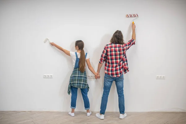 Pareja joven pintando paredes y tomados de la mano — Foto de Stock