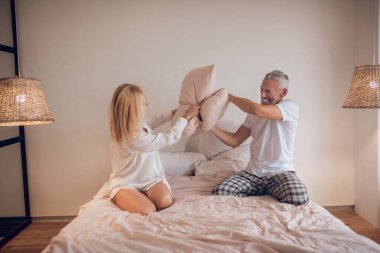 Evli çift yatak odasında eğleniyor ve yastıklarla kavga ediyor.