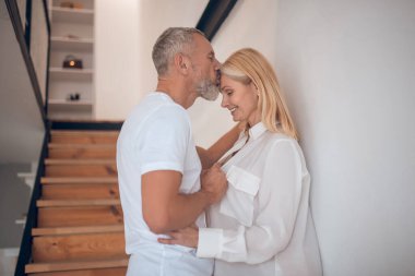 Grey-haired man standing on the stairs and kissing his wife clipart