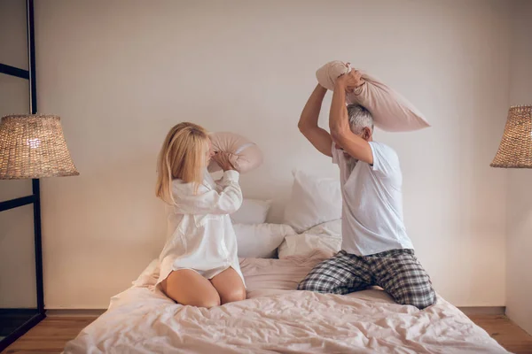 Gifta par som har roligt i sovrum och slåss med kuddar — Stockfoto