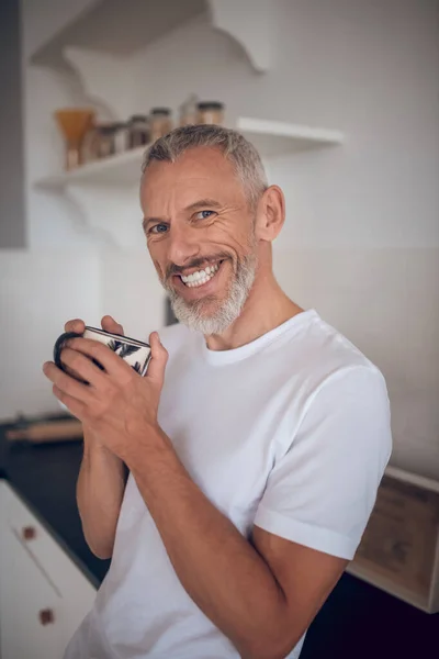 Grauhaariger großer Mann, der eine Tasse in der Hand hält und freundlich lächelt — Stockfoto