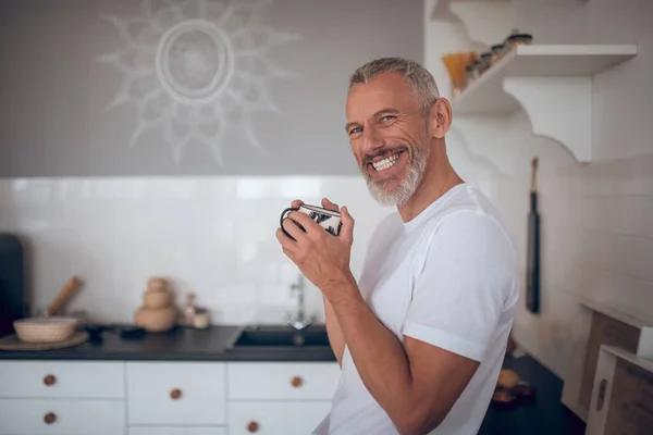 Grey-haired tall man holding a cup and smiling nicely