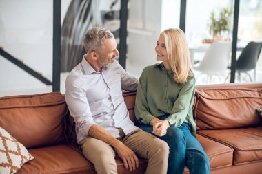 Olgun bir çift kanepede oturuyor ve neşeli bir konuşma yapıyorlar.