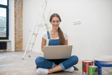 Genç bir kadın yerde oturup internette sörf yapıyor.