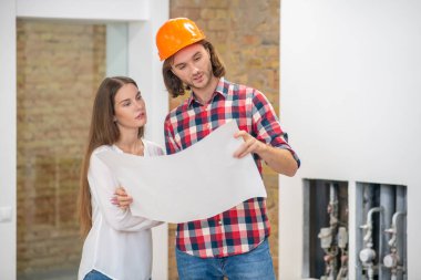 Koruyucu kasklı genç bir adam ve proje tasarımını inceleyen bir kadın müşteri.