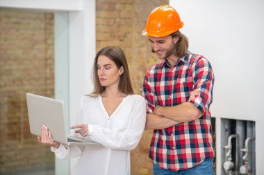 Koruyucu kasklı genç bir adam ve internetten bilgi arayan bir kadın müşteri.