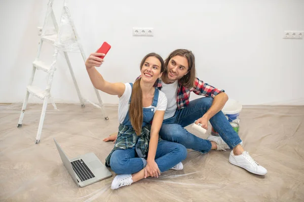 Pareja feliz sentada en el suelo y haciendo selfie —  Fotos de Stock