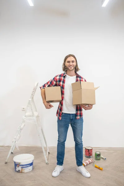 Hombre de pelo largo de pie cerca de la pared con cajas en las manos — Foto de Stock