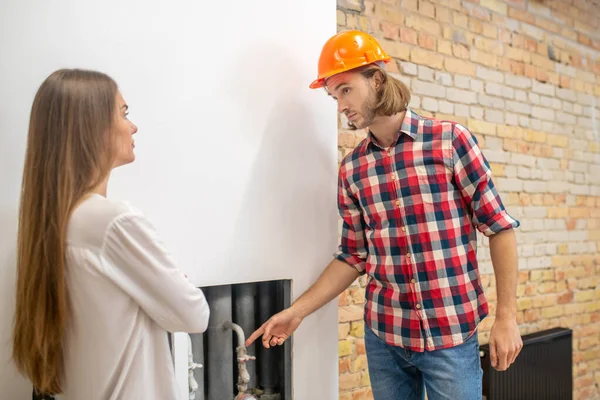 Trabajador de la construcción en casco naranja explicando algo a un cliente — Foto de Stock