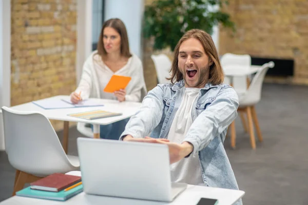 Jonge man met blond haar die achter de laptop zit en zijn handen uitstrekt — Stockfoto