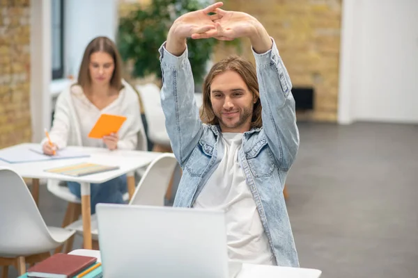 Jonge man met blond haar die achter de laptop zit en zijn handen uitstrekt — Stockfoto
