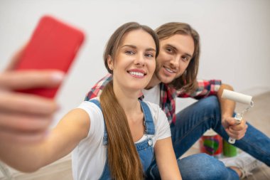 Genç mutlu çift yerde oturuyor ve selfie çekiyorlar.