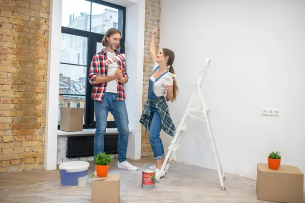 Jovem casal de pé n na sala vazia pronto para começar a pintar — Fotografia de Stock