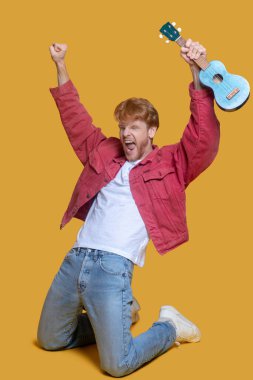 Ukulele giymiş kırmızı ceketli adam heyecanlanıyor.