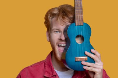 Kızıl ceketli, sakallı, yakışıklı, ukuleleli genç bir adam.