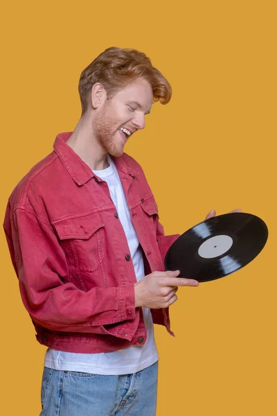 Red-haired bearded young man in red jacket with a record looking positive — Stock Photo, Image