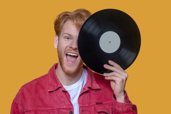 Red-haired bearded young guy in red jacket with a record — Stock Photo, Image