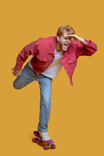 Ginger young man in red jacket with a skateboard — Stock Photo, Image