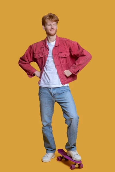 Τζίντζερ αυτοπεποίθηση νεαρός άνδρας με κόκκινο σακάκι με ένα σκέιτμπορντ — Φωτογραφία Αρχείου
