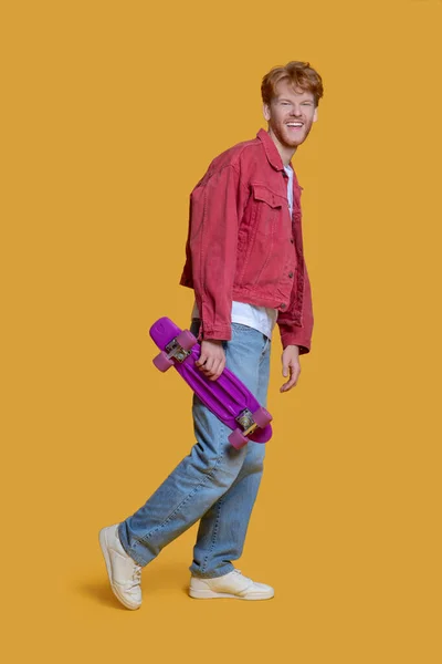 Hombre con chaqueta roja sosteniendo un monopatín y sonriendo —  Fotos de Stock