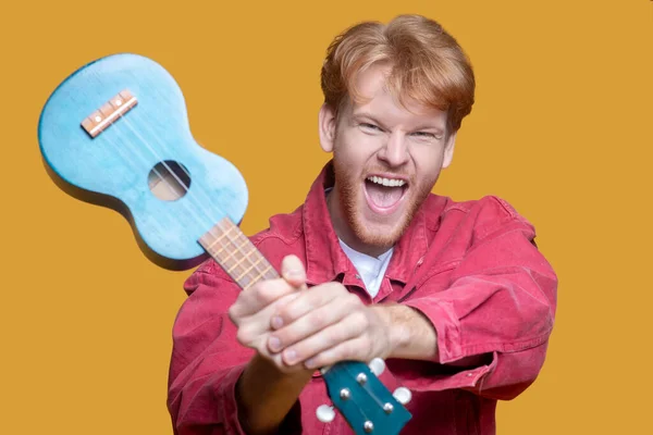 Jovem barbudo homem em casaco vermelho com ukulele — Fotografia de Stock