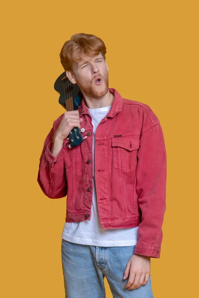 Young bearded man in red jacket with ukulele — Stock Photo, Image