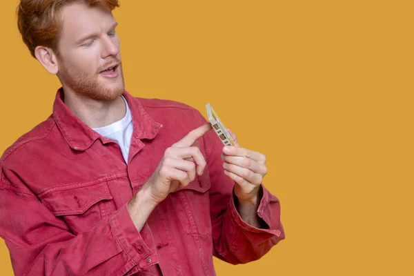Young ginger man in red jacket holding a cassette and looking interested