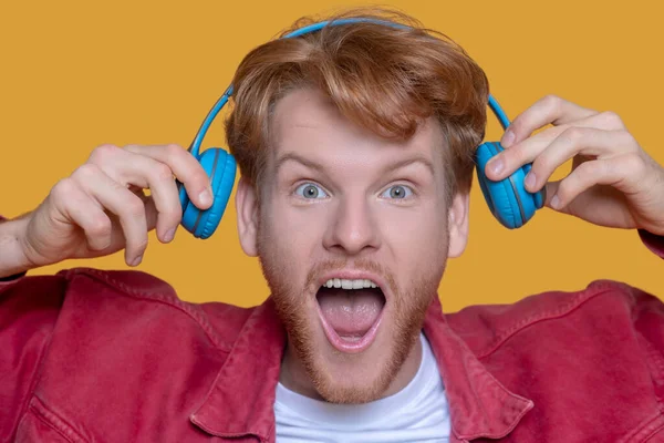 Young ginger man in red shirt with blue earphones — Stock Photo, Image