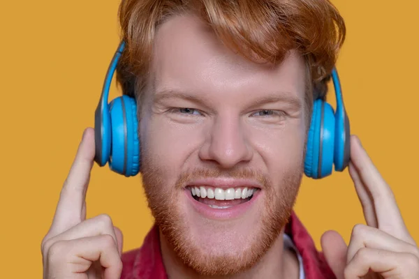 Joven jengibre escuchando música auriculares azules — Foto de Stock