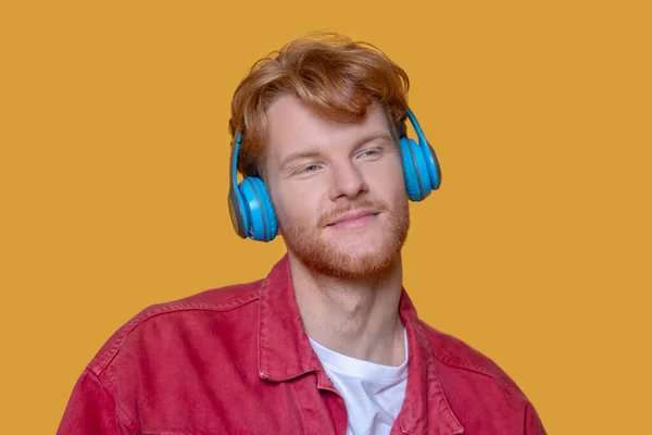 Young ginger man listening to music blue earphones — Stock Photo, Image